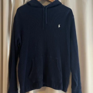 Mörkblå hoodie från Ralph Lauren - Säljer en snygg mörkblå hoodie från Ralph Lauren. Den har en klassisk design med en liten broderad logga på bröstet och en praktisk ficka framtill. Perfekt för både vardag och avslappnade tillfällen. Passar bra till höst och vinter!