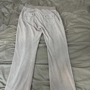 juicybyxor handukksmaterial - Superbekväma grå mjukisbyxor i loose fit med elastisk midja och snörning. Byxorna har praktiska fickor både fram och bak, perfekta för en avslappnad dag hemma eller en snabb tur till affären. Materialet är mjukt och skönt, vilket gör dem till ett måste i garderoben. Perfekt för höst och vinter!