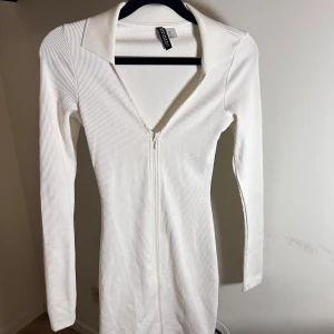 Vit ribbad klänning  - Snygg vit ribbad klänning från H&M i ett tight passform. Den har en dragkedja framtill och långa ärmar, perfekt för både vardag och fest. Klänningen är i ett mjukt och stretchigt material som formar sig fint efter kroppen. 