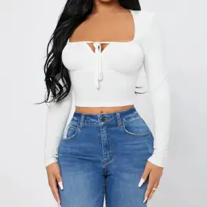 Snygg vit croppad topp med långa ärmar och knytning framtill. Perfekt för en stilren och trendig look. Passar bra till både jeans och kjol för en avslappnad eller uppklädd stil.