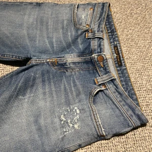 Blå jeans från Nudie - Säljer ett par tvär feta blå jeans från Nudie i mycket bra skick då jag inte använder de lika ofta längre. De har en skön passform med slitna detaljer. Storlek 29:32