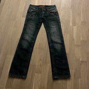 Mörkblå jeans med detaljer - Säljer ett par snygga mörkblå jeans med coola slitningar och detaljer. De är bootcut  och är perfekta för en avslappnad stil. Jeansen har knappar och dragkedja framtill samt fickor både fram och bak. Perfekta för vintern, perfekt skick och är i storlek 26, jag säljer dem så dessa är försmå för mig 💕