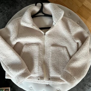 Vit teddyjacka - Supermysig  teddyjacka i mycket bra skick. Den har en dragkedja framtill och stora fickor. Perfekt för kyliga höst- och vinterdagar. Jackan är långärmad och har en normal passform men lite liten i storleken. 