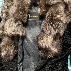 Svart pälsjacka från Anton & Moda - Säljer en elegant svart pälsjacka från Anton & Moda. Jackan har en lyxig grå riktig päls runt halsen i och svart bälte i midjan. Perfekt för kalla vinterdagar när du vill känna dig både varm och stilren. Passar till både vardag och fest! Köpt i Spanien för 450EUR säljs för bara 1500 kr