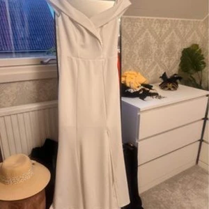 Vit långklänning med slits - Elegant vit långklänning med en stilren slits på sidan. Perfekt för sommarens fester eller en vacker bröllopsdag. Klänningen har en figurnära passform som framhäver silhuetten och ger en sofistikerad look.