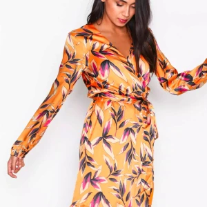 Mönstrad klänning från Gestuz - Säljer en superfin långärmad klänning från Gestuz i en härlig orange färg med blommigt mönster. Klänningen har en omlott-design och ett knytband i midjan för en smickrande passform. Perfekt för både vår och sommar! 🌸