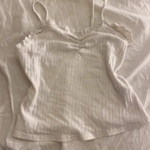Vit ribbad linnetopp - Säljer en söt vit ribbad linnetopp med smala axelband och volangdetaljer vid axlarna. Perfekt för sommardagar eller som ett lager under en kofta. Toppen är i bra skick och passar till både jeans och kjol. Superfin och enkel att matcha! 