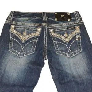 Miss Me jeans med bootcut-stil och strassdetaljer på bakfickorna. De har en cool tvättad look och är perfekta för en avslappnad men ändå stilren outfit. Passar bra till både vardag och fest!