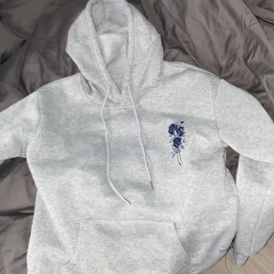 Grå hoodie med blått blommönster från Shein - Säljer en snygg grå hoodie från Shein i storlek XS. Den har ett coolt blått blommönster på bröstet och ryggen med texten 'Future Blossom'. Perfekt för en avslappnad stil och gjord i mjukt polyester. Passar bra till både höst och vår!
