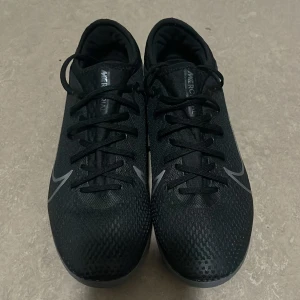 Svarta Nike fotbollsskor  - Säljer ett par svarta Nike fotbollsskor i mycket bra skick. Skorna har en snygg och stilren design med snörning och en slitstark sula. Perfekta för fotbollsträning eller match. De är bekväma och ger bra grepp på planen.