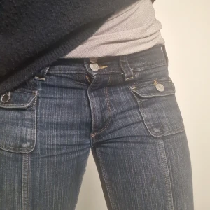 Mörkblå jeans med knappar - Säljer ett par snygga mörkblå jeans med låg midja och bootcut-stil. De har coola knappar fram och fickor med knappdetaljer. Perfekta för en avslappnad vardagslook eller en utekväll. Passar bra till både sneakers och klackar! En av knapparna har tyvärr gått av köpta för länge sen men kommer inte ihåg för hur mycket med säljer billigt