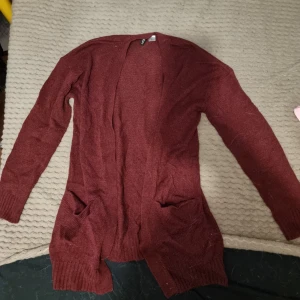 Vinröd kofta/cardigan - Mysig vinröd kofta/cardigan i stickat material. Perfekt för höst och vinter med långa ärmar och praktiska fickor framtill. Den har en avslappnad passform och är superbekväm att ha på sig. Knappt använd