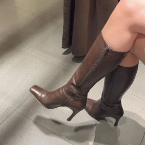 Bruna stövlar med klack - Snygga bruna stövlar i skinn med klack och dragkedja på sidan. Perfekta för höst och vinter, de ger en elegant touch till vilken outfit som helst. Passar bra till både kjol och byxor.