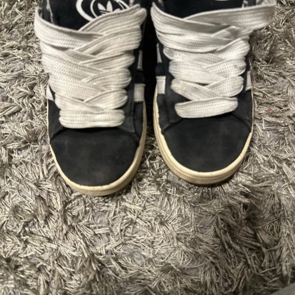 Säljer ett par svarta sneakers i bra skick med vita snören och en cool design på plösen. Perfekta för vardagsbruk och ger en skön streetstyle-look. Sulan är vit och ger en snygg kontrast till det svarta tyget.. Skor.