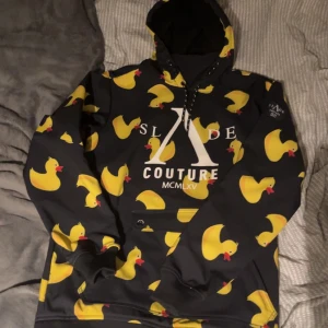 Slade Snowboard jacka  - Cool svart hoodie från Slade Couture med ett lekfullt mönster av gula ankor över hela tröjan. Den har en stor, bekväm huva och en praktisk magficka. Perfekt för att sticka ut i mängden och hålla sig varm samtidigt🐤. Den är väldigt stor i storleken så den passar de som har m och kanske L. Den är använd 2 gånger i skidbacken och är i perfekt skick, som ny. Nypris är 999