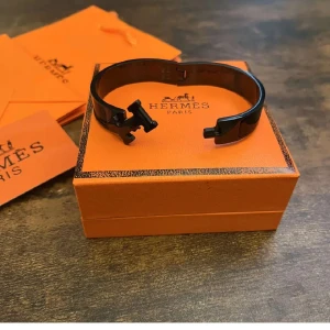 Svart armband från H - Säljer ett elegant svart armband i mycket bra skick. Armbandet har en stilren design med en metallspänne och kommer i sin originalförpackning. Perfekt accessoar för både vardag och fest!