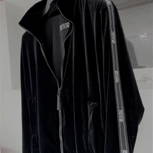 Versace Jeans Couture - Säljer en snygg svart jacka från Versace Jeans Couture. Den har en dragkedja framtill och långa ärmar med märkets logga längs ärmarna. Perfekt för en stilren look. Passar bra till både höst och vår. Obs:skriv innan köp!