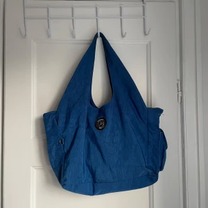 Blå axelväska från JPNY - Säljer en snygg blå axelväska från JPNY. Väskan har en praktisk design med tre stora huvudfack och en mindre ficka med dragkedja på baksidan. Perfekt för vardagsbruk eller en dag på stan. Den är i bra skick och redo för nya äventyr! 💙