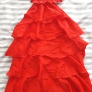 Röd volangtopp  - Säljer en superfin röd topp med flera lager av volanger. Perfekt för festliga tillfällen! Den är ärmlös och har en halterneck-design som ger en elegant look. Toppenär i bra skick och passar perfekt för sommarens alla fester.