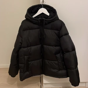 Svart pufferjacka med huva - Säljer min svarta pufferjacka från h&m då den inte kommit till användning. Endast använd ett fåtal gånger, dock så gick ena snöret som sitter längst ned av precis efter jag hade köpt den.🤍Stl M men lite oversize i modellen.☺️