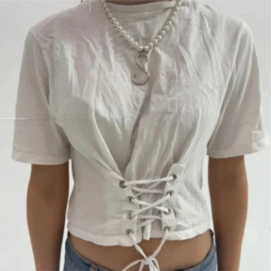 Vit kortärmad topp från Zara - Säljer en snygg vit topp från Zara i storlek S. Den har korta ärmar och en cool snörning framtill som ger en unik look. Perfekt för både vardag och fest!😚💕