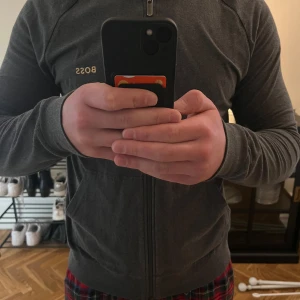 Boss zip hoodie - En mörkgrå zip hoodie från boss, med guldigt BOSS märke på vänster bröst. Väldigt bra skick, använd några fåtal gånger. Storlek M