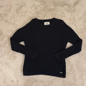 Mörkblå stickad tröja från Lexington - Säljer en stilren mörkblå stickad tröja från Lexington. Tröjan har ett klassiskt flätmönster och långa ärmar. Perfekt för kyligare dagar. Hör av dig vid funderingar och pris kan diskuteras vid snabb affär mvh Malte