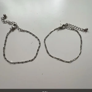 Två silverfärgade armband - Säljer två stilrena silverfärgade armband med justerbar kedja och karbinhake. Perfekta för att bära tillsammans eller var för sig för en minimalistisk look.