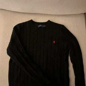 Svart stickad tröja från Polo Ralph Lauren - Säljer en stilren svart stickad tröja från Polo Ralph Lauren med kabelstickat mönster. Tröjan är storlek S och sitter väldigt bra