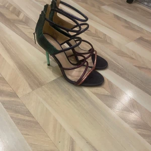 Flerfärgade klackskor från Zara - Snygga klackskor från Zara med flera remmar i olika färger, inklusive grön och röd. Skorna har en elegant klack och dragkedja baktill för enkel påtagning. Perfekta för att ge en färgklick till din outfit.