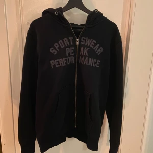 Svart hoodie från Peak Performance - Hej, jag säljer en stilig svart hoodie från Peak Performance med texten 'Sportswear Peak Performance' på bröstet. Hoodien är väldigt bekväm och i toppskick då den inte har nå defekter eller fläckar. Pris kan diskuteras. 