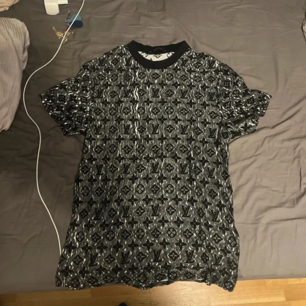 Säljer en snygg t-shirt från Louis Vuitton med ett unikt mönster i svart och grått. T-shirten är kortärmad och tillverkad i Italien. Perfekt för dig som vill ha något stilrent och exklusivt i garderoben.. T-paidat.