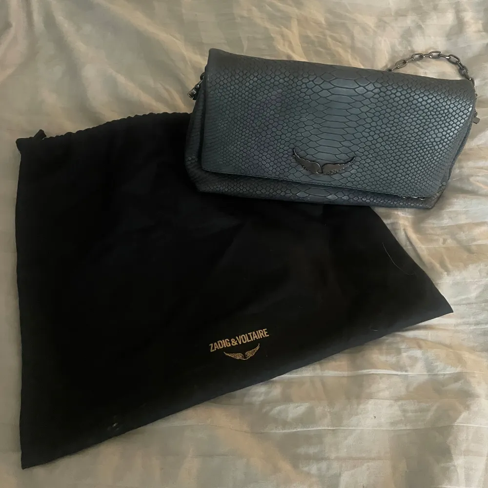 Snygg svart axelväska från Zadig & Voltaire med ett coolt ormskinnsmönster. Väskan har en kedjerem och en dekorativ detalj på framsidan. Använd fåtal gånger och själva påsen är sönder men annars är allt som nytt . Laukut & Käsilaukut.