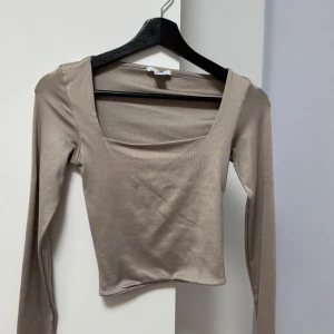 Beige långärmad topp från Amisu - Säljer en stilren beige långärmad topp från Amisu. Toppen har en fyrkantig urringning och är tillverkad i ett mjukt, stretchigt material som ger en bekväm passform. Perfekt för att matcha med både jeans och kjol.