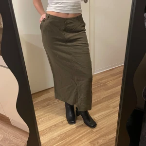 Olivgrön långkjol från Almina - Snygg olivgrön långkjol från Almina med en stilren design. Kjolen har en dragkedja framtill och knappar i midjan för en säker passform. Perfekt för en avslappnad och chic look. Ingen storlek i den men jag är 160cm och när XS