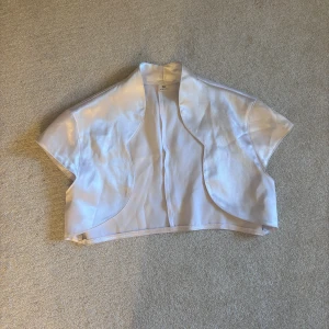 Vit kortärmad bolero - Snygg vit bolero med korta ärmar och en öppen design. Perfekt för att lägga till en elegant touch till din outfit. Den har en glansig finish som ger en lyxig känsla. Säljer pågrund av flytt och för mycket kläder 😄😄