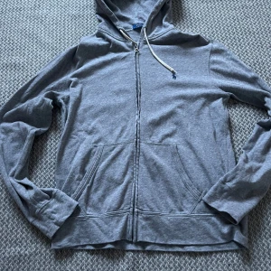 Grå hoodie från Polo Ralph Lauren - Säljer en stilren grå hoodie från Polo Ralph Lauren med dragkedja och broderad logga på bröstet. Tröjan har långa ärmar och en praktisk huva med snörning. Perfekt för en avslappnad look. Priset är inte hugget i sten 