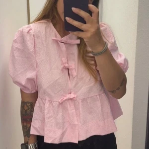 Rosa blus  -  rosa blus med puffiga kortärmar och rosett knytning framtill. Blusen har en luftig passform och en lätt textur som ger en söt och feminin look. Perfekt för våren/sommaren eller i skolan/fest! Aldrig använd tyvärr, bara provad!🥰