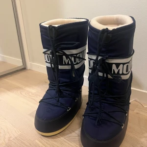 Moon Boots - Snygga och varma marinblå Moon Boots med vit text och snörning. Perfekta för skidresor.