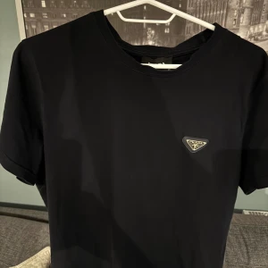 Svart t-shirt från Prada - Snygg svart t-shirt från Prada med en diskret logga på bröstet. Perfekt för en stilren look. T-shirten har korta ärmar och en klassisk passform.