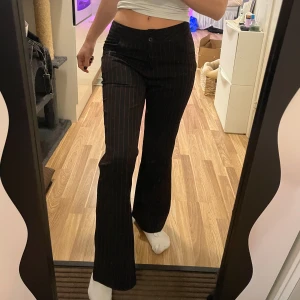 Svarta randiga kostymbyxor  - Snygga svarta byxor med tunna röda ränder. De har en låg midja och en bootcut-stil som ger en trendig look. Jag är 160cm lång 