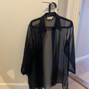Svart transparent blus från Cop Copine - Snygg svart transparent blus från Cop Copine. Den har långa ärmar och knappar framtill. Perfekt för en stilren och modern look.