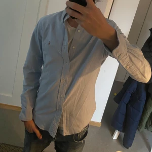 Blå skjorta från Ralph Lauren - Säljer just nu en snygg blå skjorta från Ralph Lauren i slim fit. Skjortan har långa ärmar och är dekorerad med det klassiska broderade logotypen på bröstet. Perfekt för en stilren look. Ny pris runt 1600 mitt pris 599. Skicket är 9/10. Säljer då den har blivit lite för liten. Skulle passa någon runt 173-183. Skriv för fler frågor eller bilder. Passar perfekt till jeans eller till linnebyxor. Priset kan alltid diskuteras vid snabb affär.🤩 Färgen syns i bild 4.