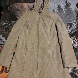 Beige manchesterkappa från Vero Moda - Säljer en stilren beige kappa från Vero Moda i mjukt manchestertyg. Jackan har en huva och dragkedja framtill, perfekt för kyliga dagar. Den har långa ärmar och två fickor på sidorna. En klassisk och tidlös design för garderoben.