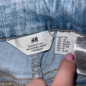 Bootcut jeans från H&M - Snygga ljusblå bootcut jeans från H&M med justerbar midja och låg midja. De har en klassisk femficksdesign och stängs med dragkedja och två knappar. Perfekta för en avslappnad stil.