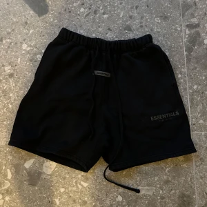 Svarta shorts från Essentials - Snygga svarta shorts från Essentials med elastisk midja och snörning. Perfekta för en avslappnad stil. Essentials-logga på benet ger en stilren touch. Ej äkta