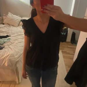 Svart blus med spetsdetaljer - Snygg svart blus med spetsdetaljer på ärmarna. Blusen har en v-ringad design och korta ärmar med spets detaljer 💯