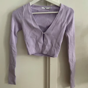 Ljuslila ribbad topp från NA-KD - Säljer en ljuslila ribbad kofta från NA-KD. Den har en v-ringad design med en knapp framtill och är croppad. Endast provad men aldrig använd. (Andra bilden är från NA-KD’s hemsida) 