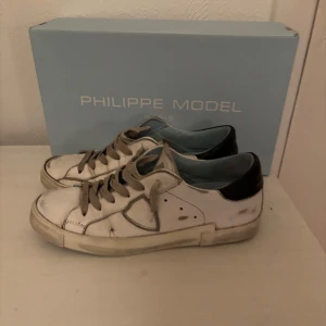 Vita sneakers från Philippe Model, storlek39-40 - Snygga vita sneakers från Philippe Model med svarta detaljer på hälen. Skorna har en klassisk design med snörning och en diskret logga på sidan. Perfekta för en stilren look. Storlek 39-40, con 8/10