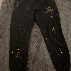 Mörkblå byxor med färgstänk från Gallery Dept - Unika mörkblå byxor från Gallery Dept med coola färgstänk i olika färger. Byxorna har en avslappnad stil med tryck på ena benet och snörning i midjan. Perfekta för en trendig och konstnärlig look. Priser kan sänkas. Helt Nya.